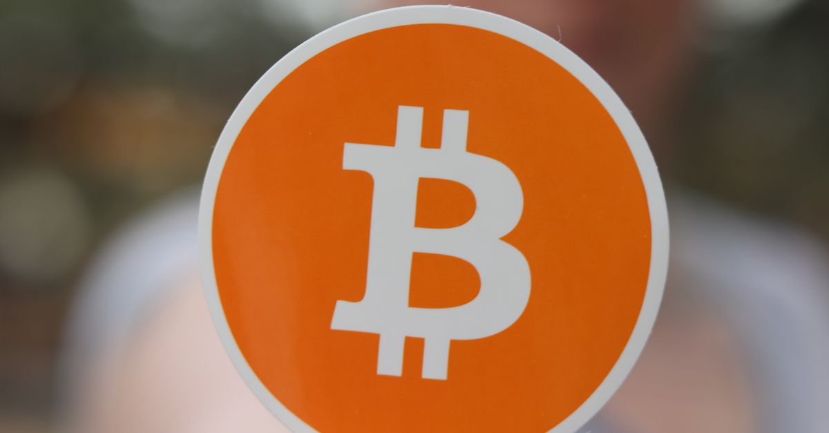 A person holds a Bitcoin logo sticker with a blurred background, showcasing cryptocurrency themes.